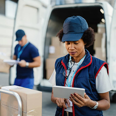 Delivery worker in uniform checking a tablet with packages and a delivery van in the background for amazon wholesale supplier distribution services"